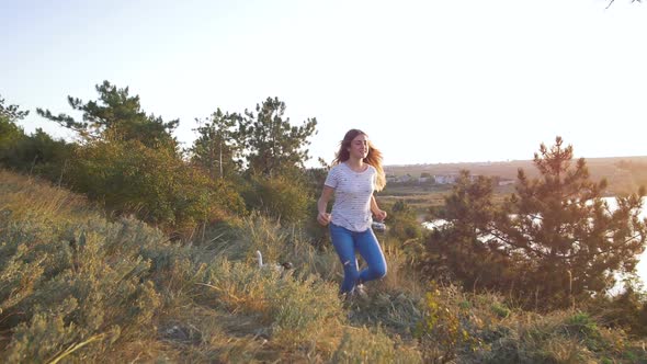 Young Attractive Woman Playing with a Dog Jack Russell in the Meadow at Sunset with Sea Background