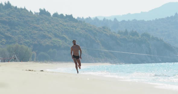 The Handsome Man with a Perfect Athletic Body in Swimming Trunks Having Fun on a Deserted Beach in