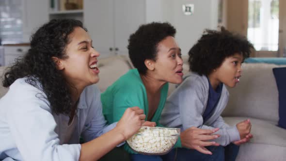 Mixed race lesbian couple and daughter watching tv eating popcorn