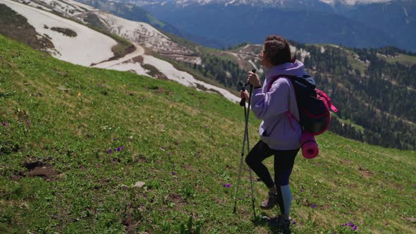 Female Climber is Hiking in Mountains Moving Up Over Slope Helping to Herself By Trekking Poles