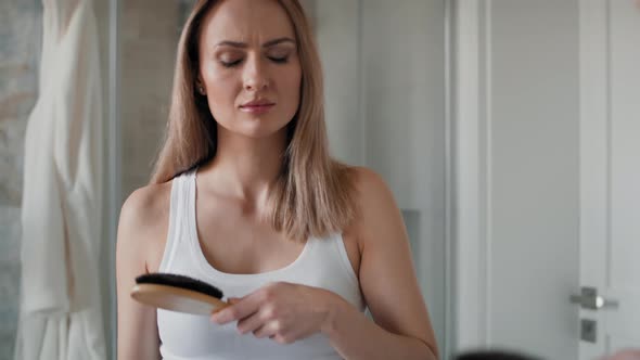 Caucasian woman brushing hair in the bathroom and looking at their loss on the brush. Shot with RED