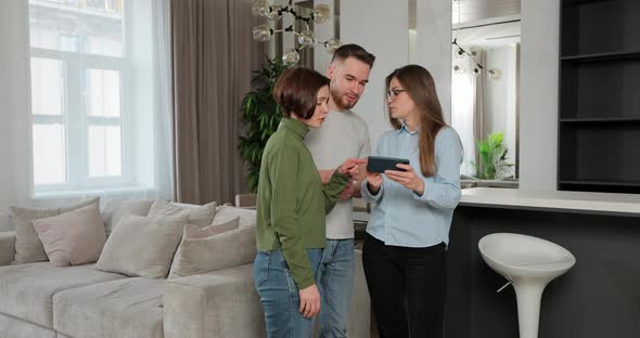 Couple Standing in New House Talking to Woman Real Estate Sales Manager Who is Using Tablet Showing