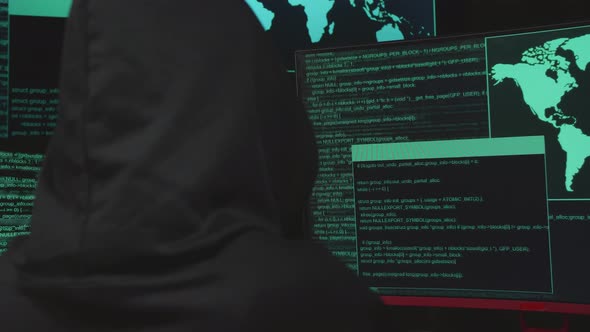 Back View Of Hacker Hacking With Multiple Computer Screens In Dark Room