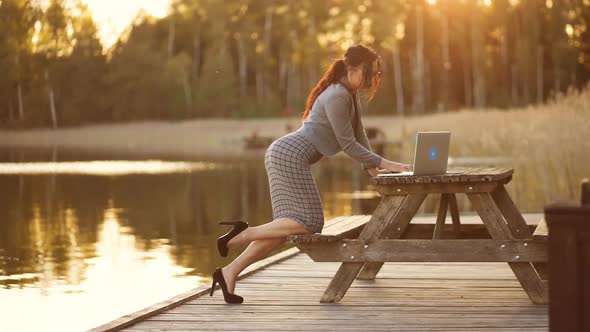 Sexy Business Woman in Formal Suit and High Heels Bends Over and Uses Laptop Outdoors During