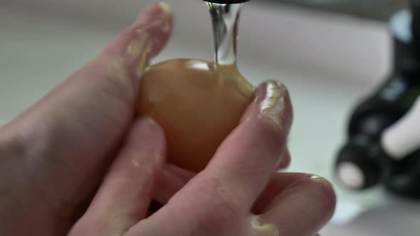 Woman washing chicken eggs under water at kitchen