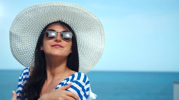 Medium Closeup Portrait of Beauty Travel Woman in White Hat and Sunglasses Posing at Sea Background