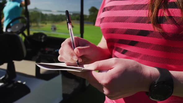 Two caucasian women playing golf one writing in a notebook