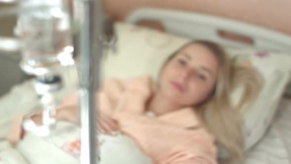 Young Woman Looks at Infusion Bottle on the Stand in the Hospital