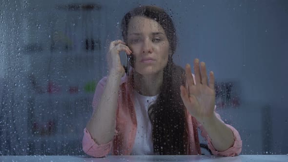 Woman Talking Phone and Looking Through Rainy Window, Waiting Husband at Night