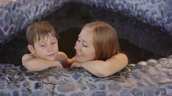 Young Woman and Her Son Relax in a Stone Bath Filled with Healing Herbal Infusions