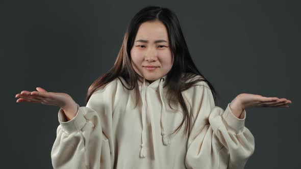 Asian Unsure Girl in White Hoodie Shrugs Her Arms, Makes Gesture of I Don't Know
