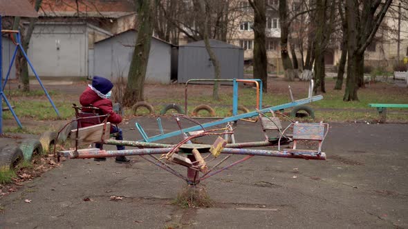 A Boy in a Medical Mask Is Spinning on an Old Carousel