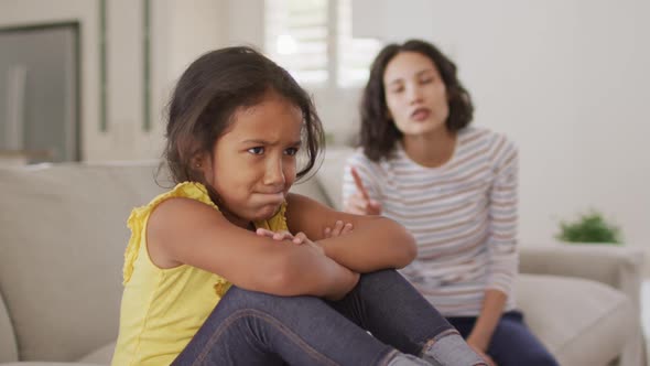 Angry hispanic mother telling off her young updet daughter sitting on sofa