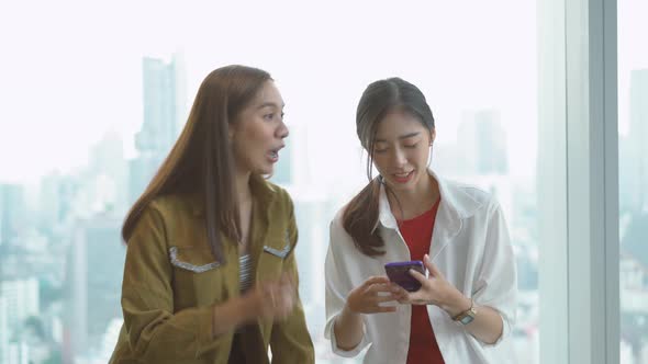 Colleagues two young women talking and making selfie at phone sitting together, laughing smile 