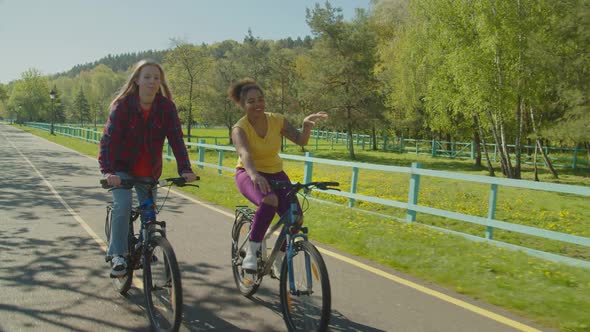 Joyful Diverse Hipster Women Having Fun Racing on Bikes in Public Park