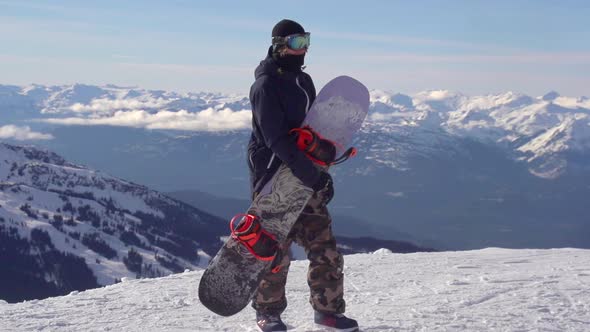 A young man snowboarder standing with his snowboard on a snow covered mountain.