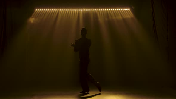 Ballroom Dancer Guy Moves Gracefully on Stage. Dark Silhouette in Soft Yellow Lighting. Slow Motion.