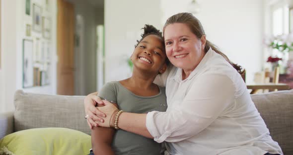 Portrait of happy caucasian woman and her african american daughter smiling in living room