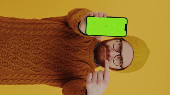 Vertical Shot of a Caucasian Middleaged Man Pointing to His Smartphone with Green Screen