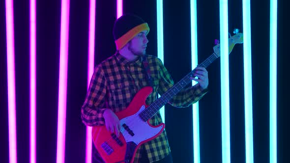 An Excited Guitarist Plays an Electric Guitar in the Studio Surrounded By Pink and Blue Neon Tubes