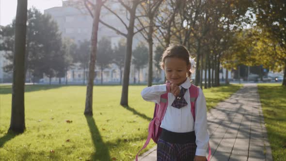 A Little Girl in School Uniform Is Walking and Talking on Smart Watches