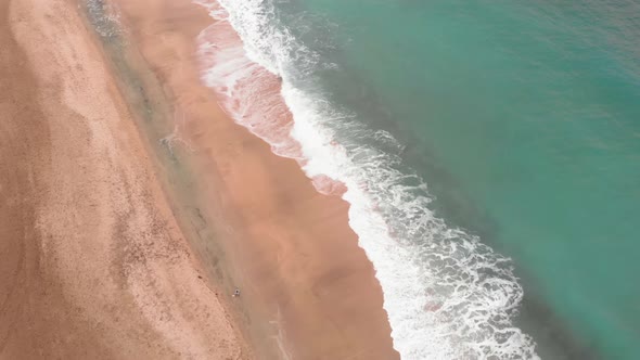 Golden beach with deep blue ocean water and white foam, aerial drone view