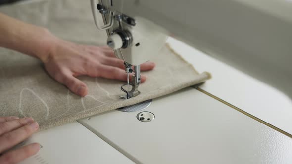 Closeup of a Young Woman's Hands Sewing Beige Fabric with a Design