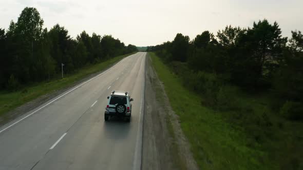 Aerial View of a Car Driving Along the Road Among Fields of Green Grass