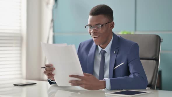 Young African Businessman Celebrating Success While Reading Documents in Office