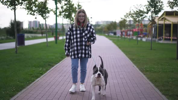 Wide Shot Portrait of Confident Beautiful Young Woman and Dog Walking in City in the Evening in Slow