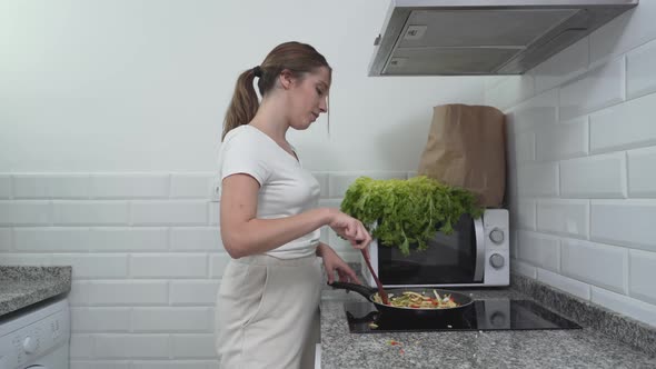 Young Woman Cooking Vegetable Dish On Electric Gas Stove In Her Apartment