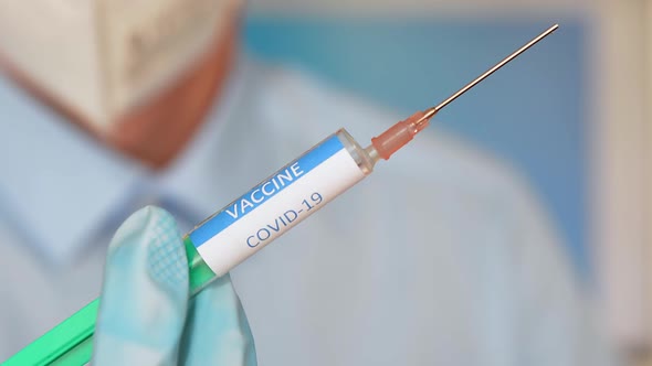 Close up of a researcher with face mask holding a syringe with coronavirus vaccine