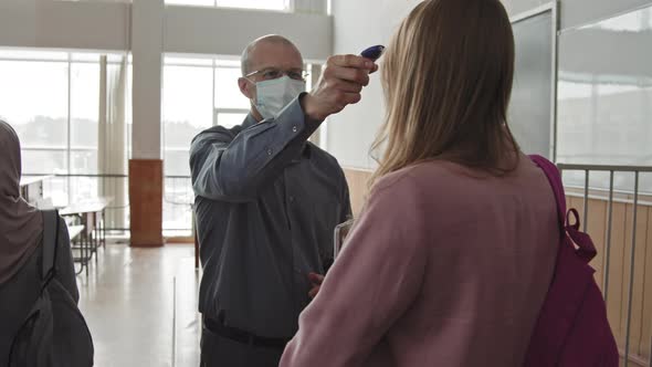 Male Professor Measuring Students Temperature in Auditorium