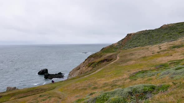 Shot of cliff by the sea, trail along the calm sea, grey day, green grass