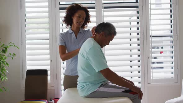 Mixed race female physiotherapist helping senior man massaging his back