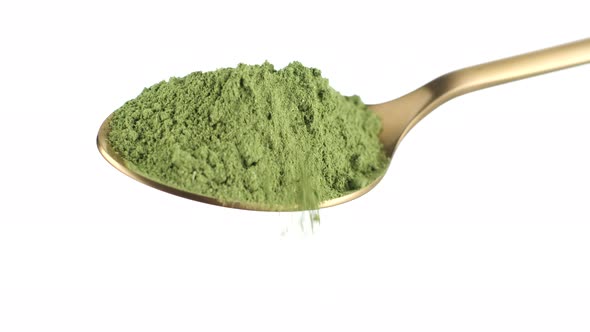 Pour spirulina or moringa green powder from a golden spoon. isolated on white background