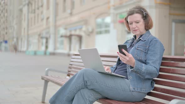 Old Woman Using Smartphone and Laptop While Sitting Outdoor on Bench