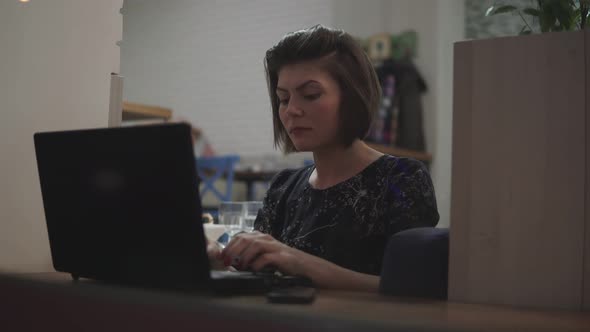 Young Business Woman Sitting By the Window with a Laptop and Working