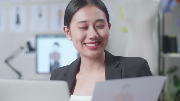 Close Up Of Smiling Asian Female Designer In Business Suit Looking At The Paper In Hand