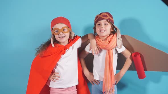 Two Playful Caucasian Children in Pilot Suit, Cloak and Cardboard Airplane Stand Together