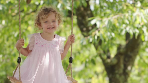 Spring and happy summer time. Joyful smiling little girl swinging on the swing, child with blue eyes