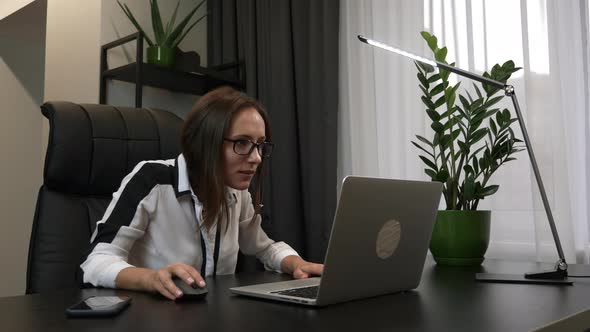 Smiling businesswoman is working on laptop, happy about her successful work and raising hands up