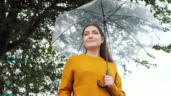 Woman in a Mustard Sweater Stands Under a Transparent Umbrella in Rainy Cold Weather