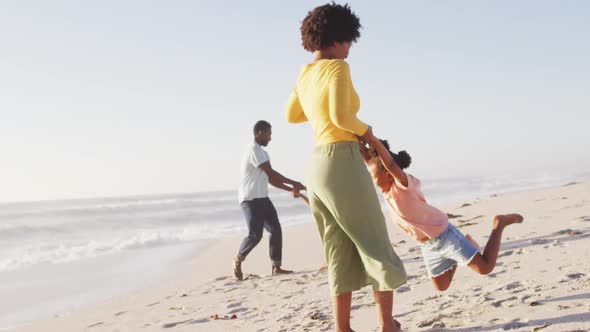 Smiling african american family holding hands and playing on sunny beach