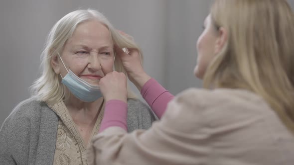 Portrait of Old Female Retiree Sitting at Home As Senior Woman Putting on Covid19 Face Mask on