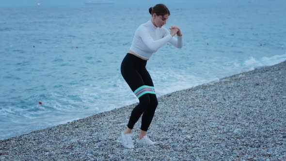 Fitness Outdoors  a Woman Doing Fitness Exercises Using Elastic Band on the Pebble Beach