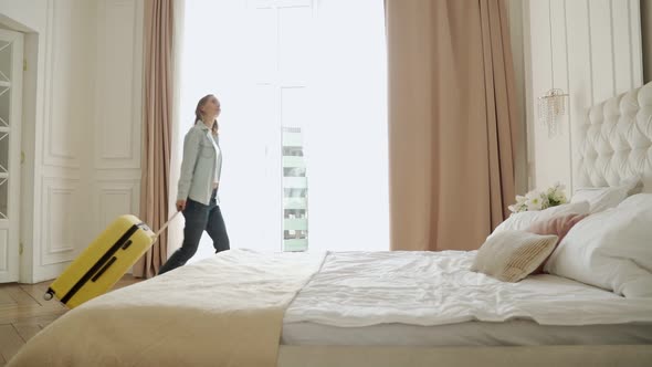 Woman Walking Into a Hotel Room with Suitcase and Fell on Bed Tired