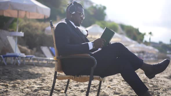 Portrait of Confident Elegant African American Man Reading Book Listening to Music in Headphones