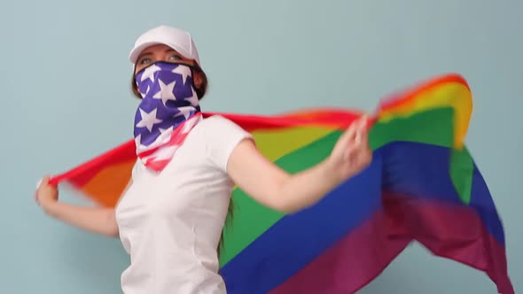 Woman of Caucasian Ethnicity in a White Cap and Tshirt and USA Mask Waving the LGBT Flag
