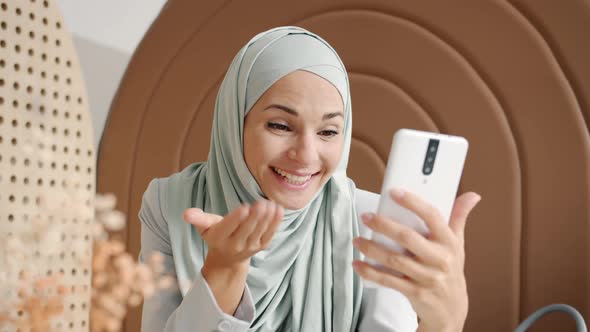 Joyful Hijabi Lady Chatting and Gesturing Making Online Video Call From Cozy Cafe